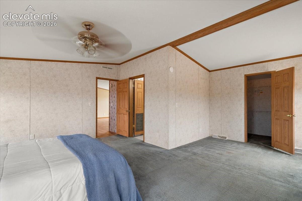 Vaulted ceiling with wood-finish beam, ceiling fan with light fixture, gray carpet, and wood-panel doors