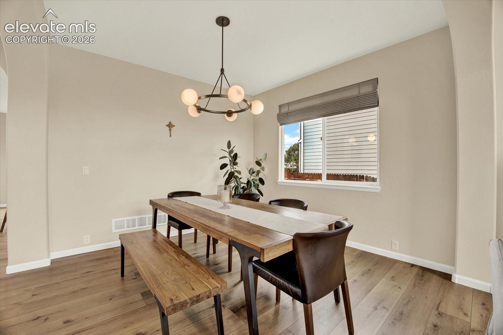 Architectural archways, wood-finish flooring, a contemporary multi-globe chandelier, and a large picture window with integrated blinds
