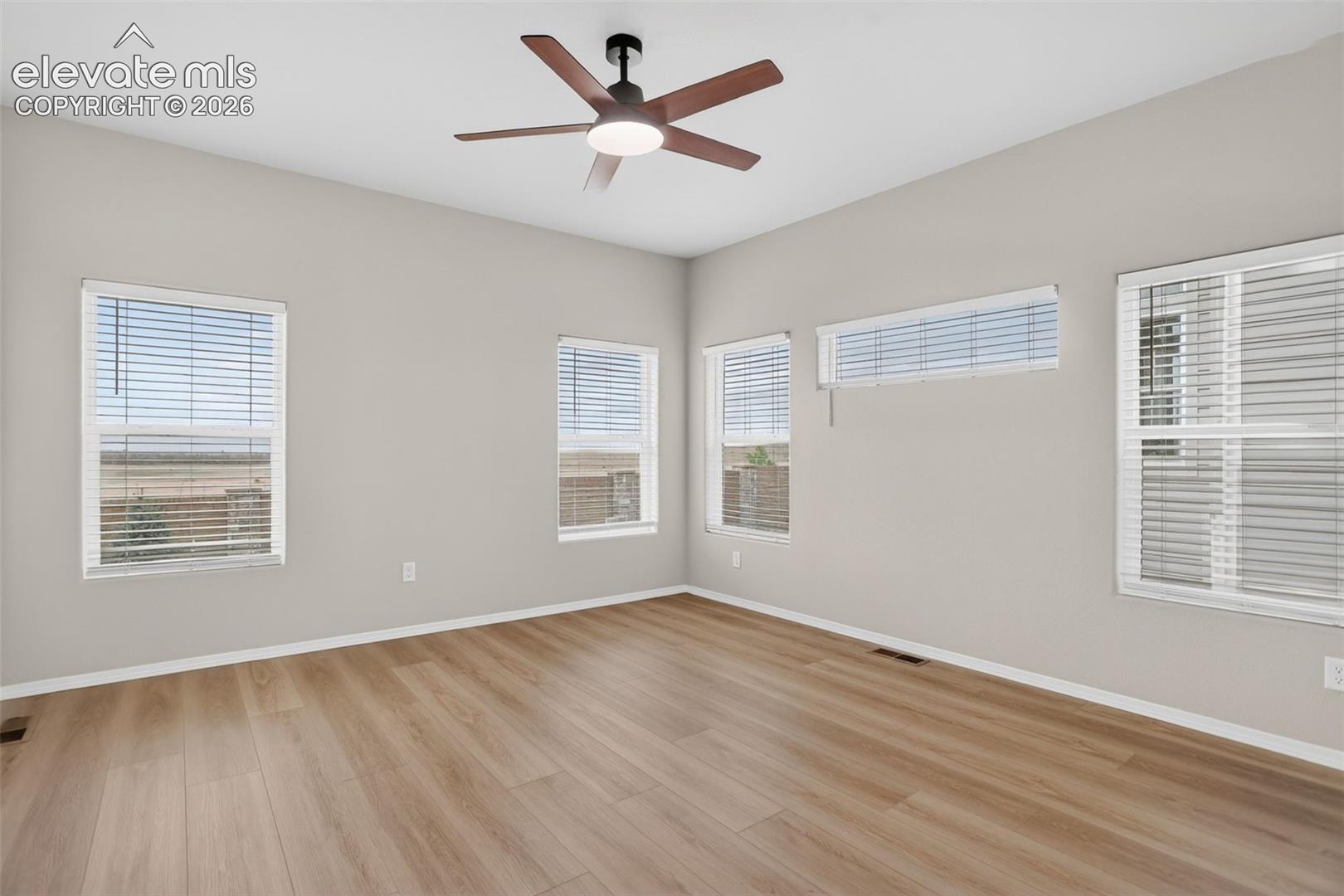 Spacious room featuring wood-finish flooring, a contemporary ceiling fan with integrated lighting, and multiple windows providing ample natural light