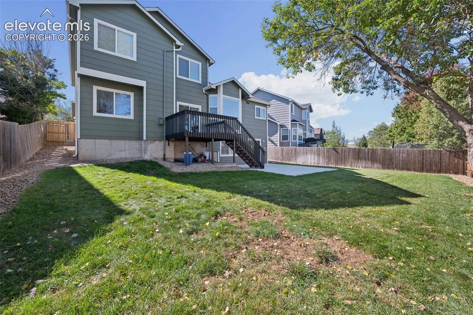 Two-story exterior with horizontal siding, elevated rear deck with staircase, concrete patio, and fenced backyard