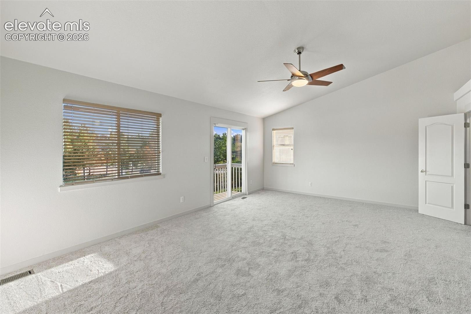 Vaulted ceilings, neutral carpeting, a central ceiling fan with integrated lighting, dual-pane windows with horizontal blinds, and a sliding glass door