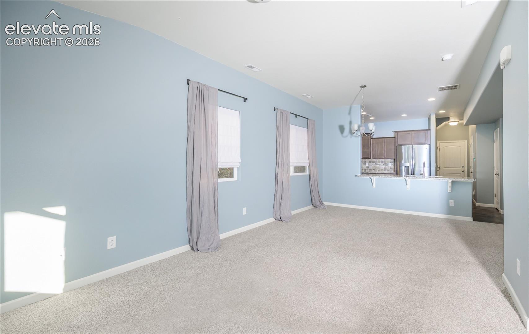 Open-concept interior featuring light blue walls, neutral carpeting, recessed lighting, and a kitchen peninsula with a breakfast bar