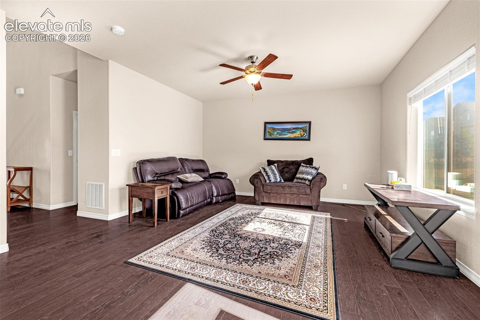 Spacious living area featuring wood-finish flooring, a ceiling fan, and large windows