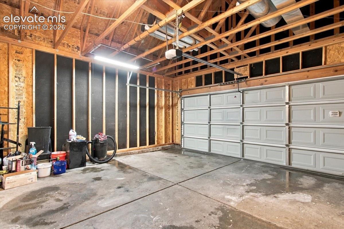 Two-car garage featuring a concrete floor, sectional overhead door, exposed wood-frame trusses, and integrated lighting fixtures