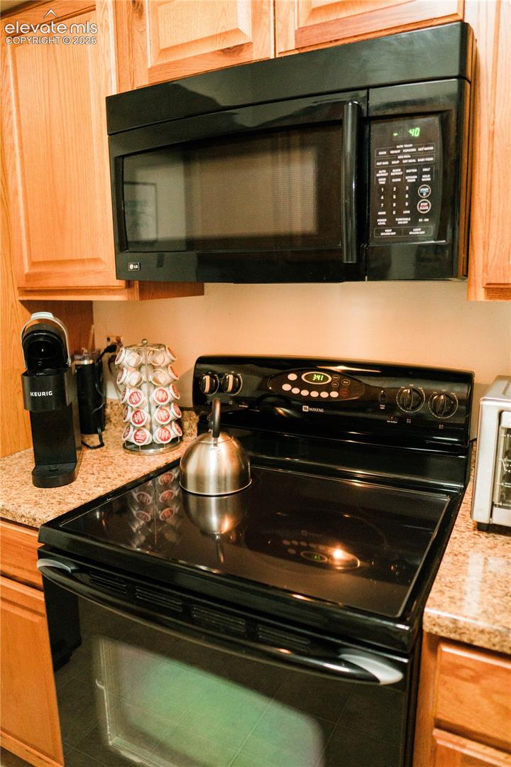 Built-in black microwave, black electric range with an oven, granite-finish countertops, and wood cabinetry