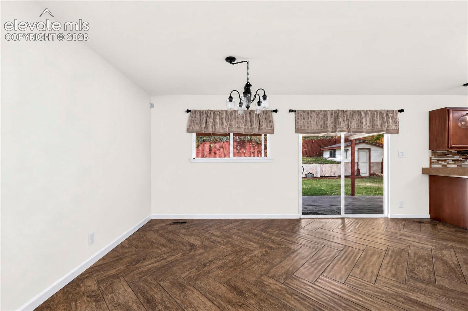 Herringbone wood-finish flooring, sliding glass door, overhead chandelier, and built-in wood cabinetry