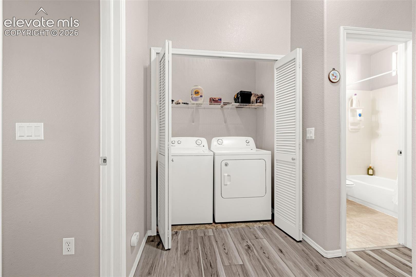 Dedicated laundry area featuring bifold louvered closet doors, built-in wire shelving, and wood-finish flooring