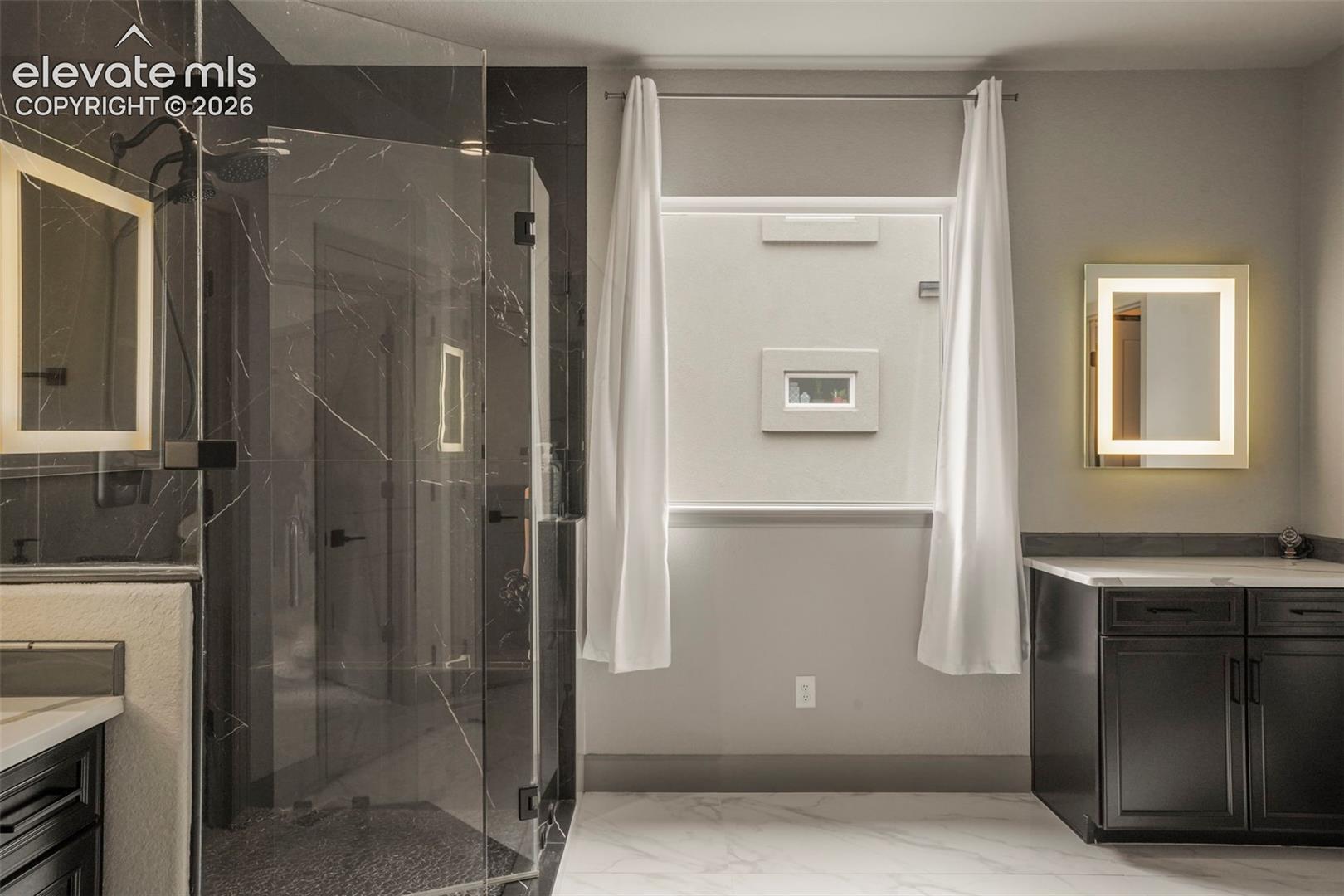 Modern bathroom showcasing a spacious glass-enclosed shower with dark marble-finish walls and a rainfall showerhead