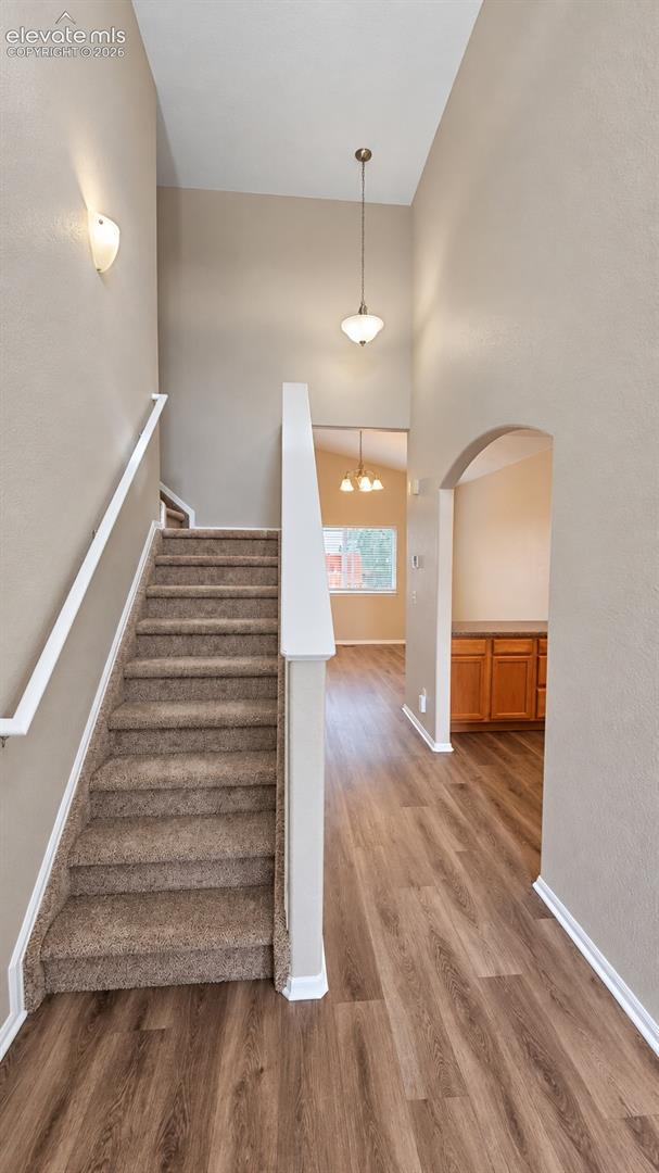High-ceiling foyer featuring wood-finish flooring, a carpeted staircase with white handrails, arched architectural detailing, and pendant lighting