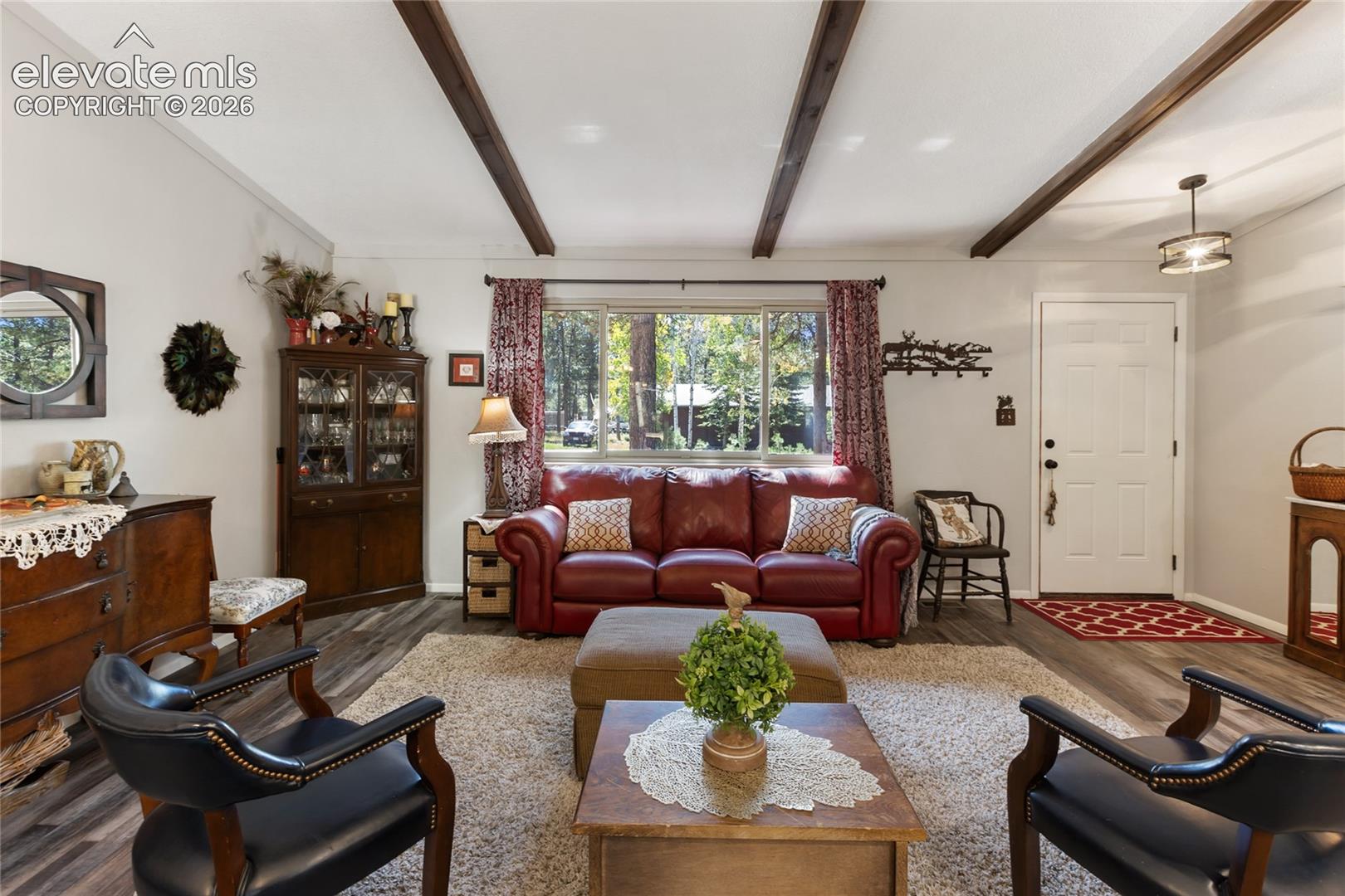 Exposed ceiling beams, wood-finish flooring, white paneled entry door, and a prominent window