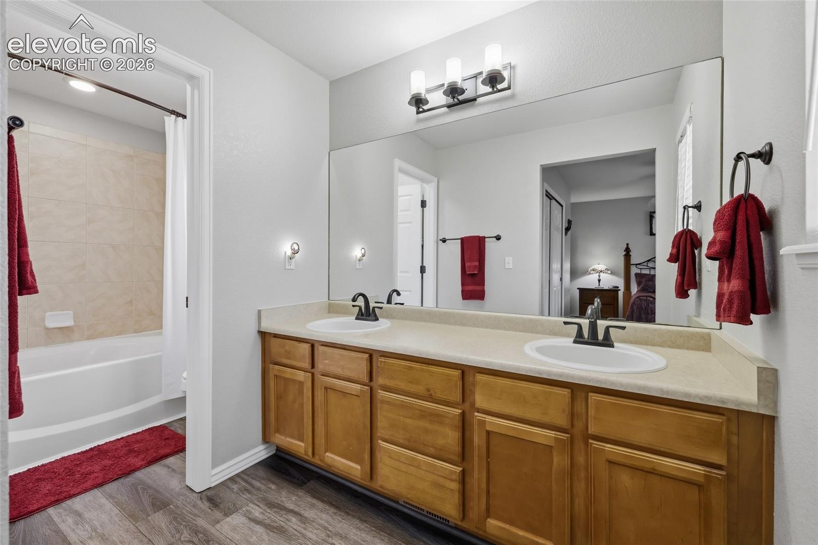 Double vanity with wood-finish cabinetry, a large wall-mounted mirror, and a full-size bathtub with tile surround
