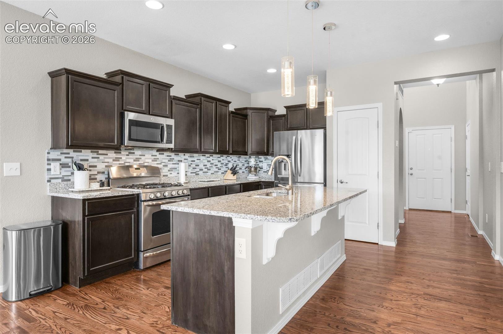 Kitchen featuring dark wood-finish cabinetry, stainless steel appliances, a tile backsplash, and a central island with a sink