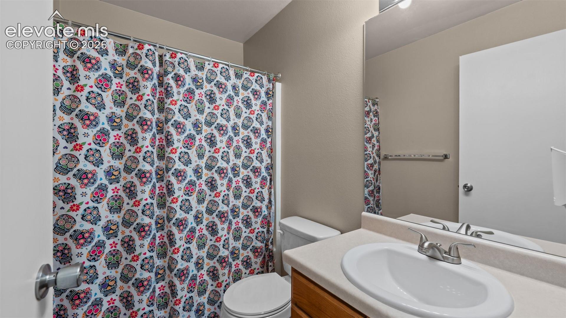Bathroom featuring a vanity with an integrated sink, wood-finish cabinetry, a wall-mounted mirror, and a toilet
