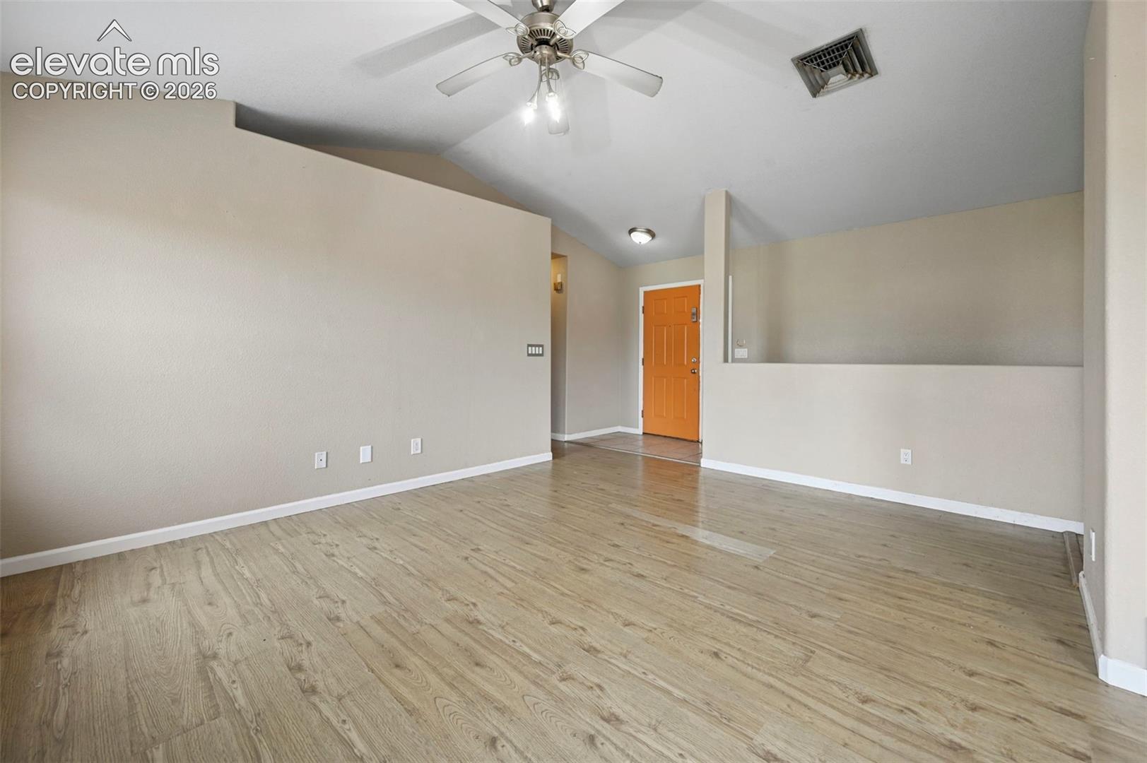 Spacious room featuring wood-finish flooring, vaulted ceiling, and a ceiling fan with integrated lighting