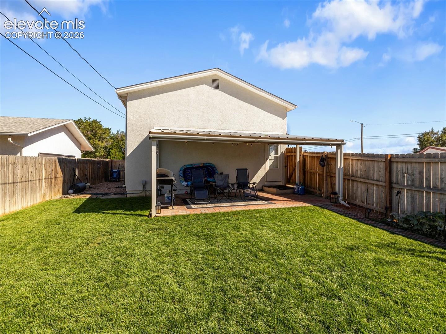 Spacious backyard featuring a covered patio with brick paving, a manicured lawn, and wood privacy fencing