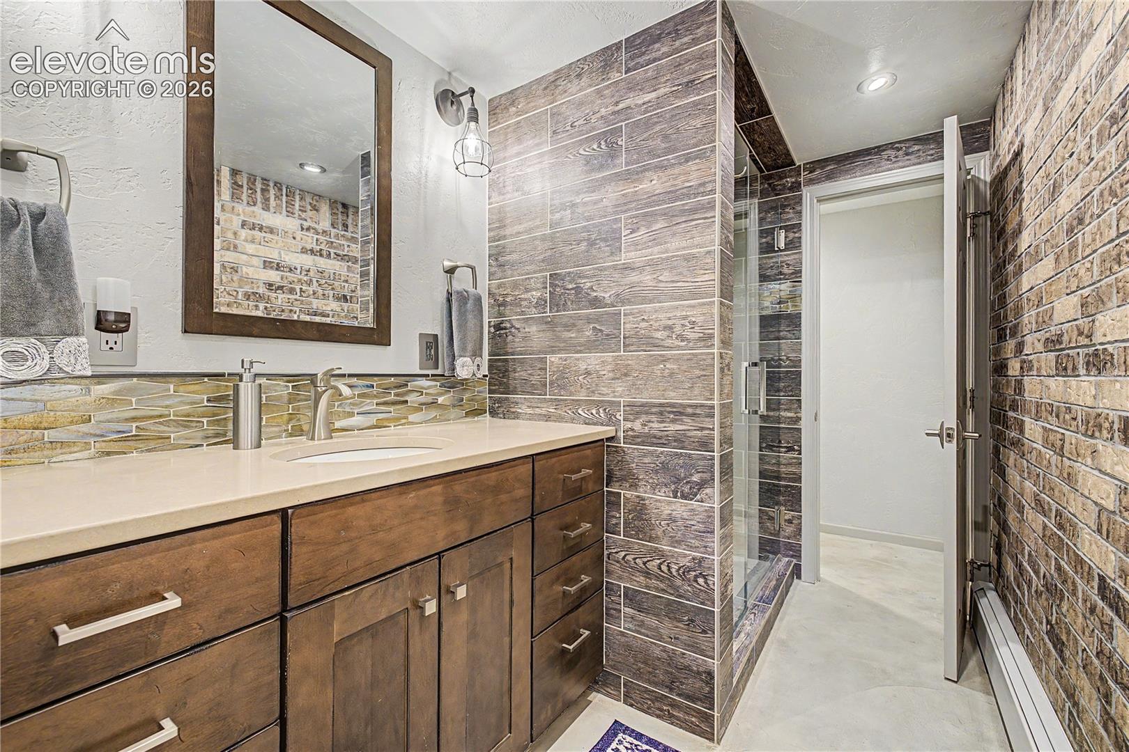 A secondary bath features a wood-look tile walk-in shower and glass-mosaic backsplash, bringing a spa-like calm to this part of the home.