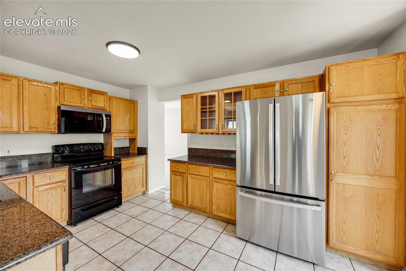 Kitchen featuring oak-finish cabinetry, stone-surface countertops, tile flooring, and stainless steel refrigerator
