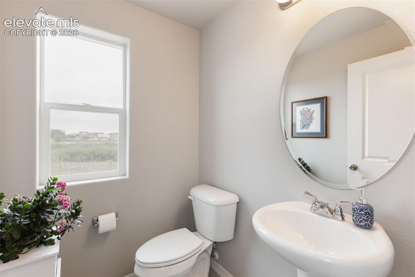 Neutral wall tones with a window, a toilet, and a pedestal sink featuring a chrome faucet