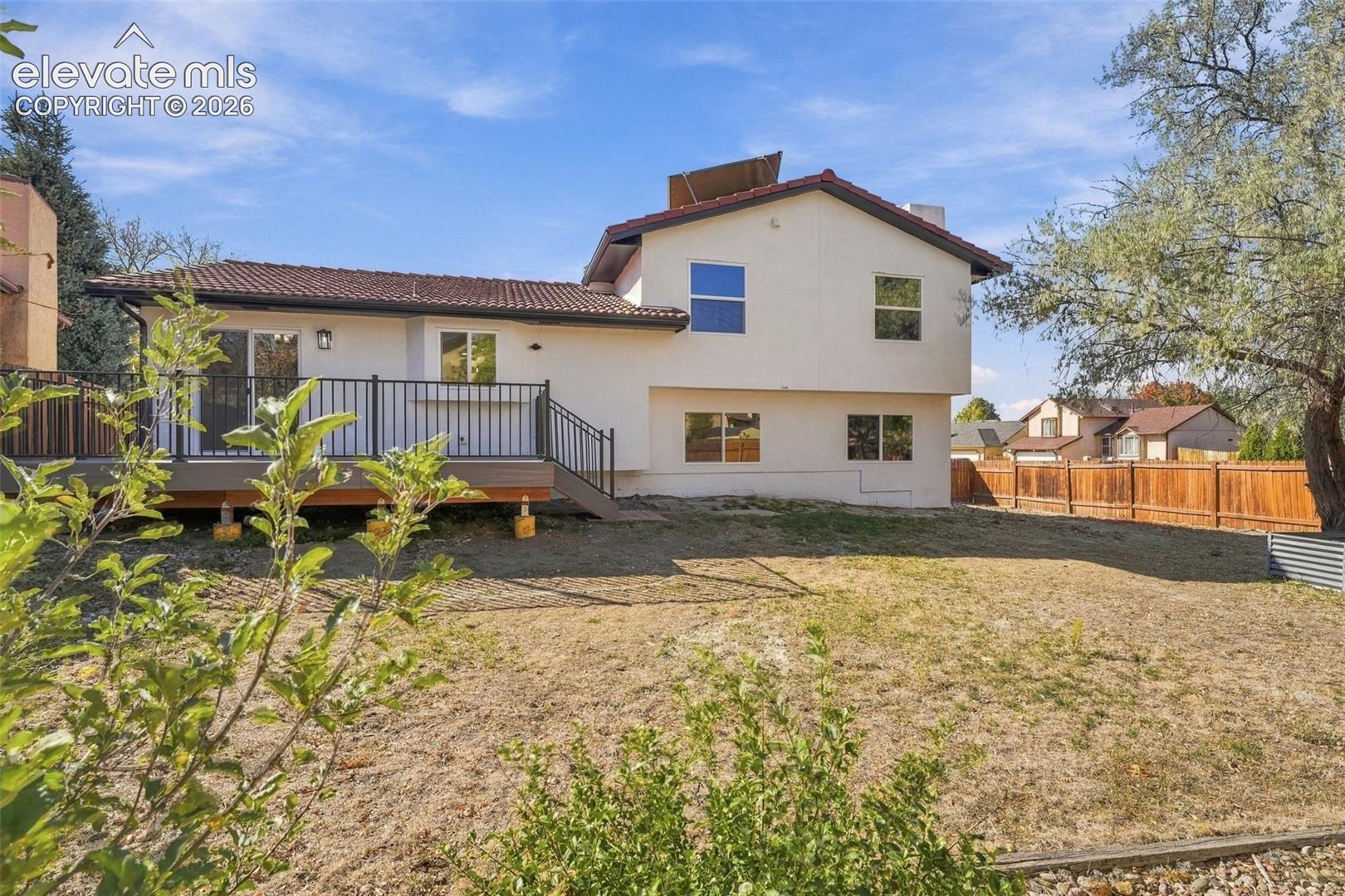 Two-story residence featuring a tile roof, light-toned exterior finish, elevated deck with black metal railing, and a wood privacy fence