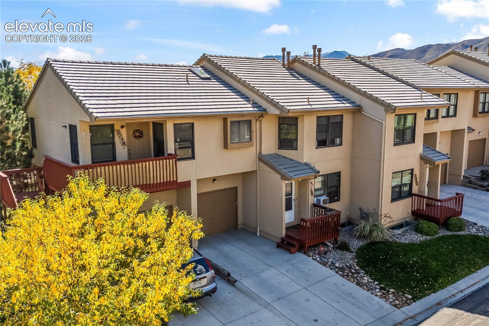 Stucco exterior with a tile roof, an upper-level balcony, a ground-level deck, and an attached garage