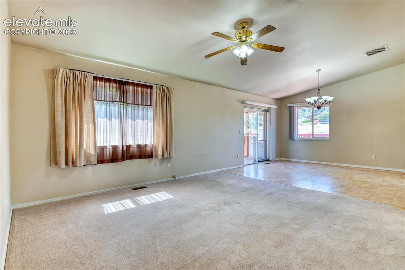 Vaulted ceiling featuring a central lighted ceiling fan, expansive windows, sliding glass door, and multi-textural stone-finish and carpeted flooring