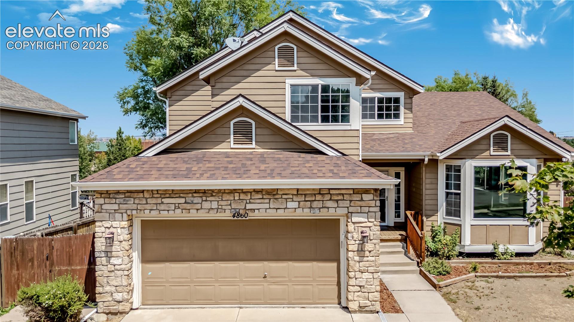 Two-story residence featuring a stone and siding exterior, an attached two-car garage, and a stepped entry with a wood railing