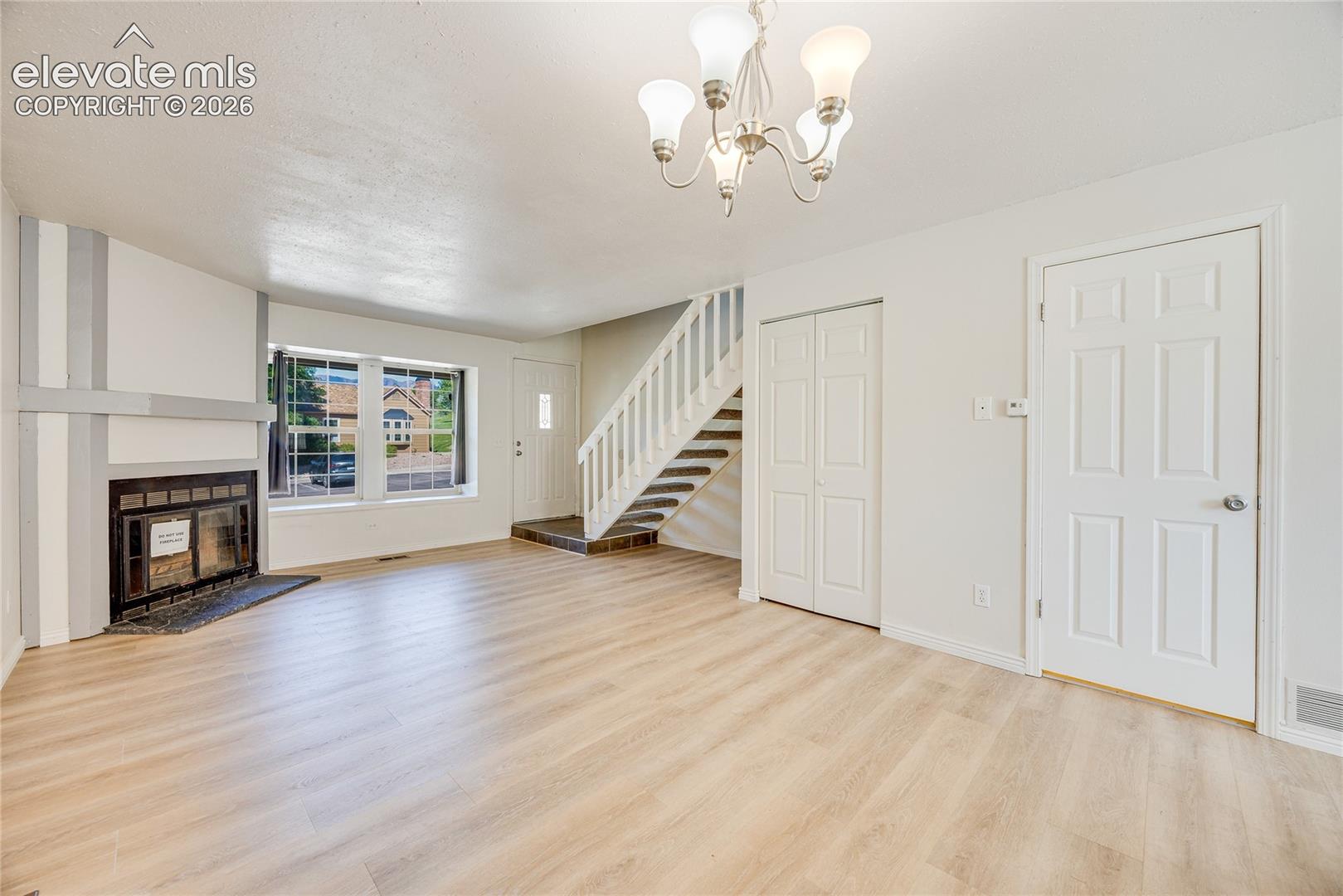 Spacious living area featuring light wood-finish flooring, a fireplace with a dark surround, and a classic chandelier