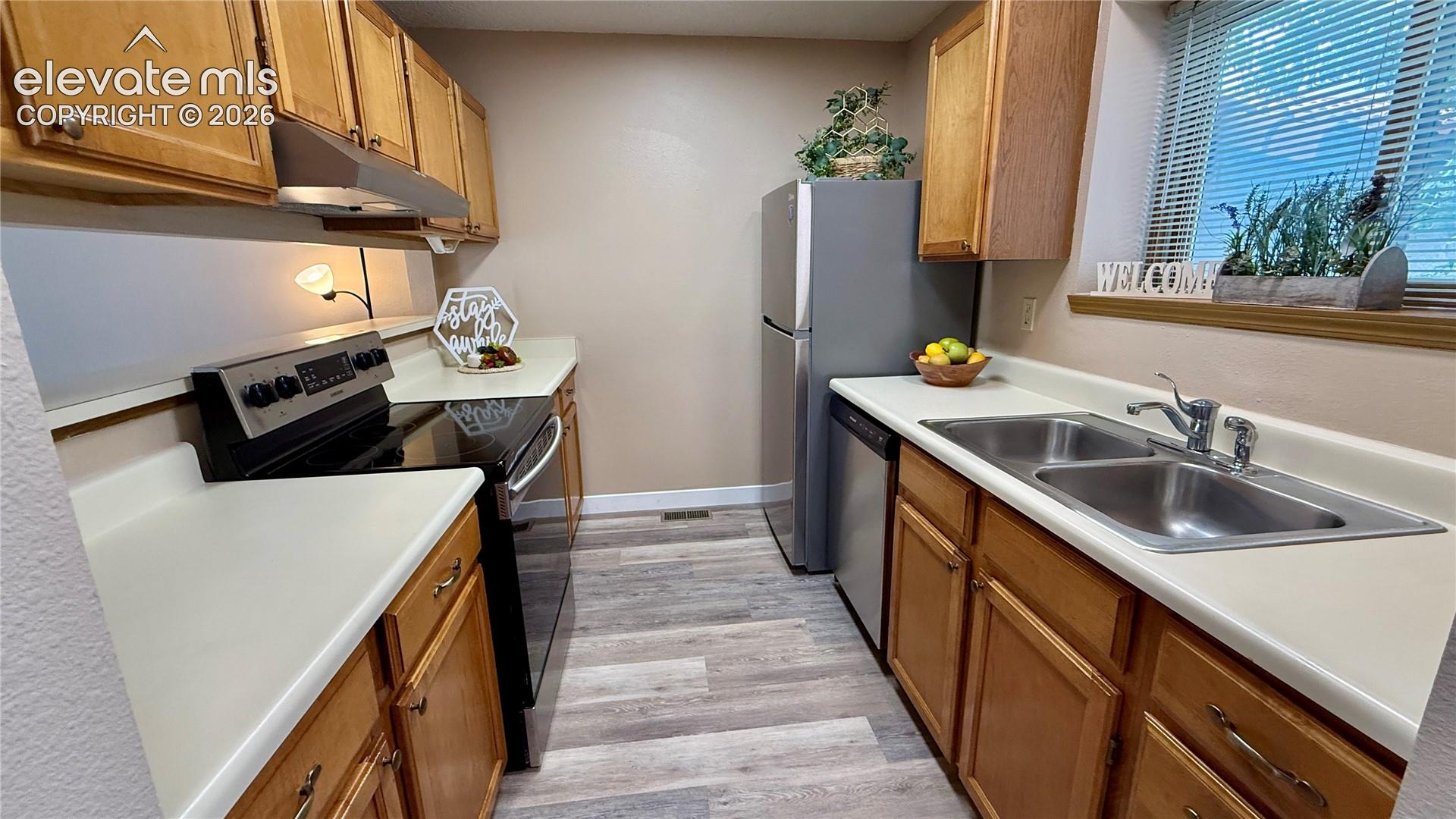 Kitchen featuring wood cabinetry, light colored countertops, wood-look flooring, dual-basin stainless steel sink, and NEW stainless steel appliances