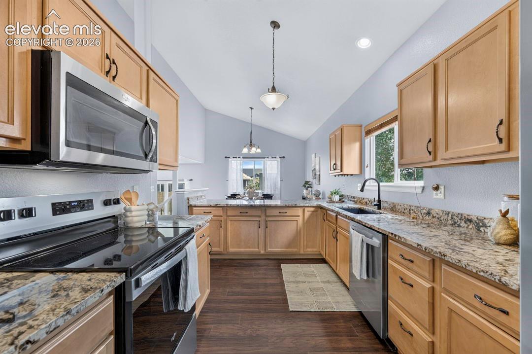 Kitchen featuring shaker-style cabinetry, stone-finish countertops, stainless steel appliances, wood-finish flooring, and a vaulted ceiling