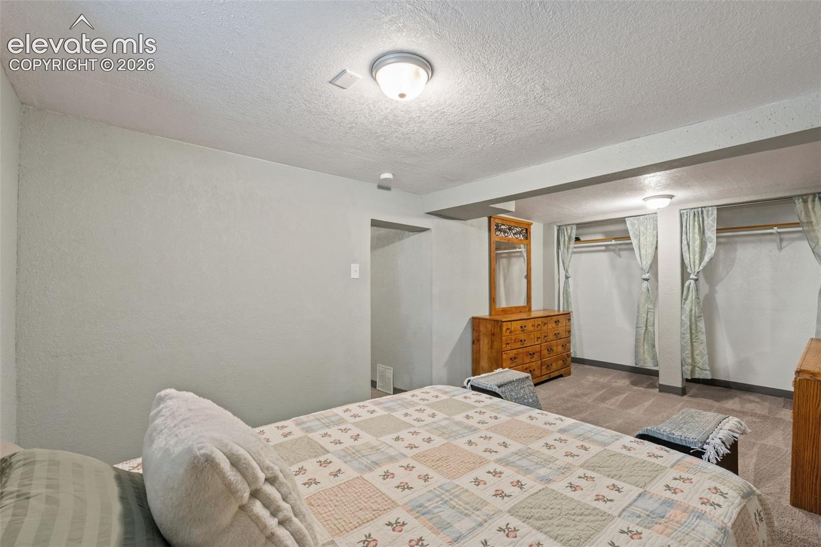 Carpeted bedroom area featuring recessed open closets with curtain coverings, a built-in ceiling light fixture, and a textured ceiling