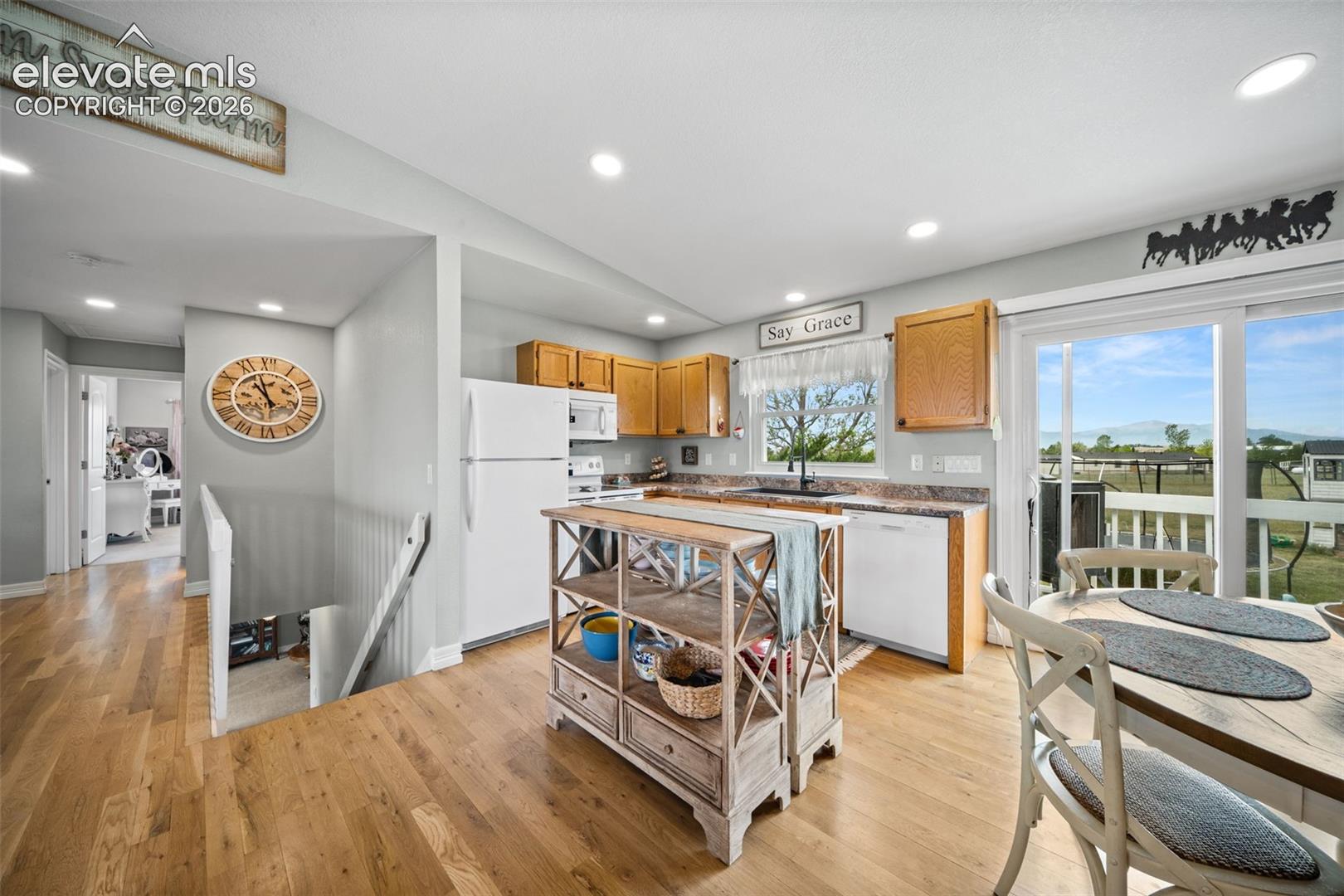 Open-concept kitchen featuring wood-finish flooring, recessed lighting, wood cabinetry, and white appliances