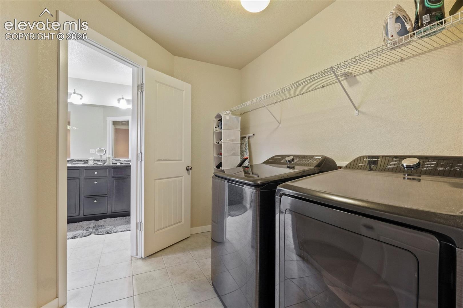 Upper Level: Dedicated laundry area featuring tile flooring and overhead wire shelving