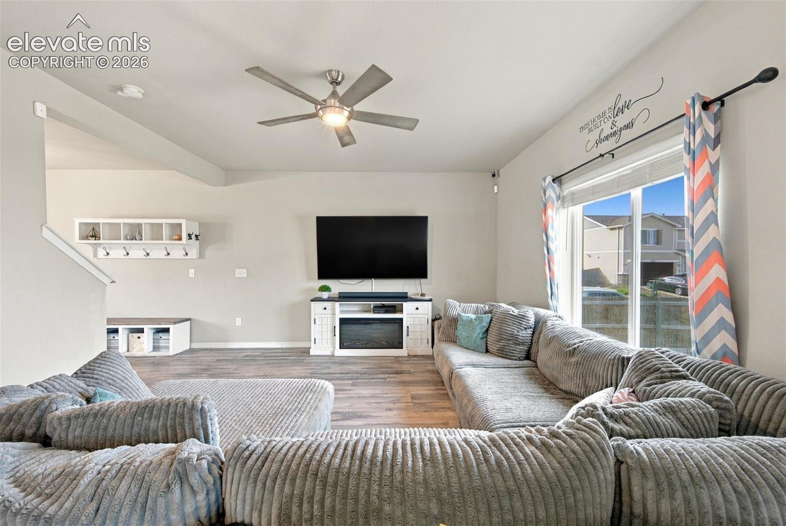 Living area featuring wood-finish flooring, a ceiling fan with integrated lighting, a white built-in fireplace console, and a wall-mounted white mudroom-style coat rack with cubbies