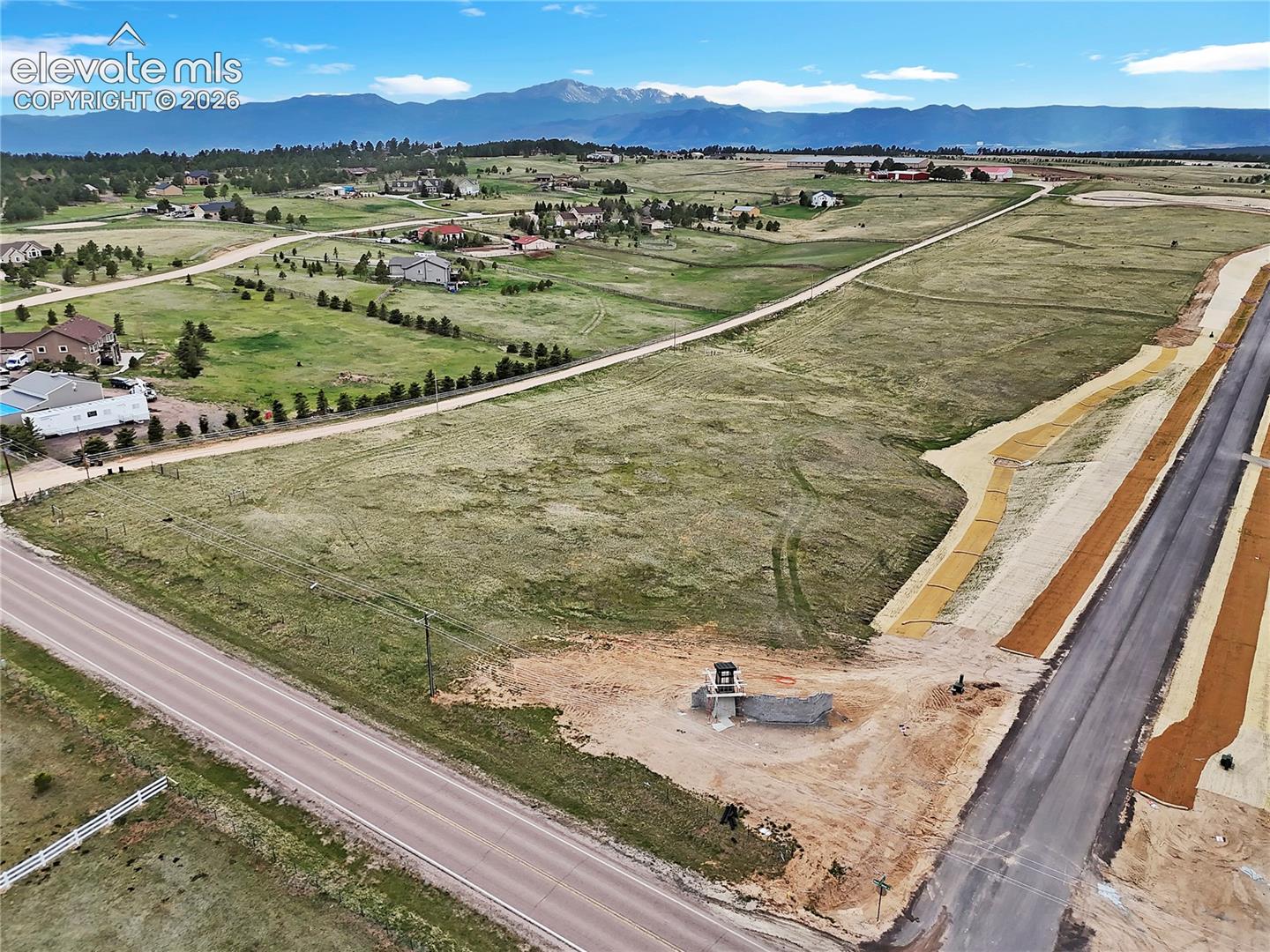 Expansive corner parcel of land featuring mountain scenery, asphalt-paved road access, and cleared ground