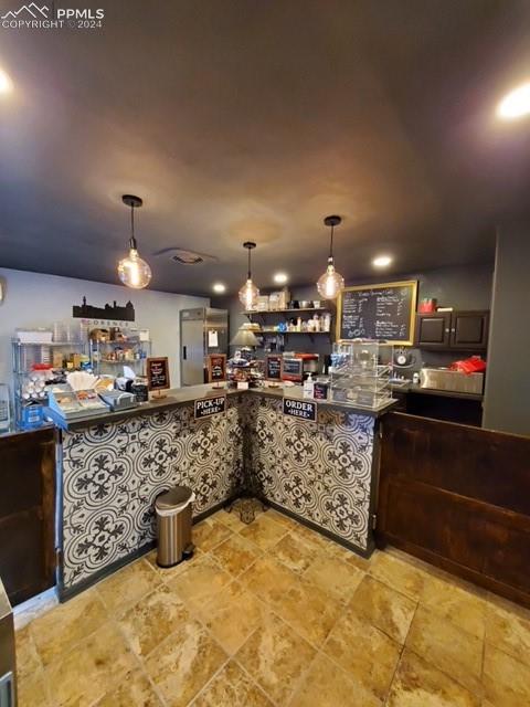 Bar featuring dark brown cabinets, hanging light fixtures, and fridge