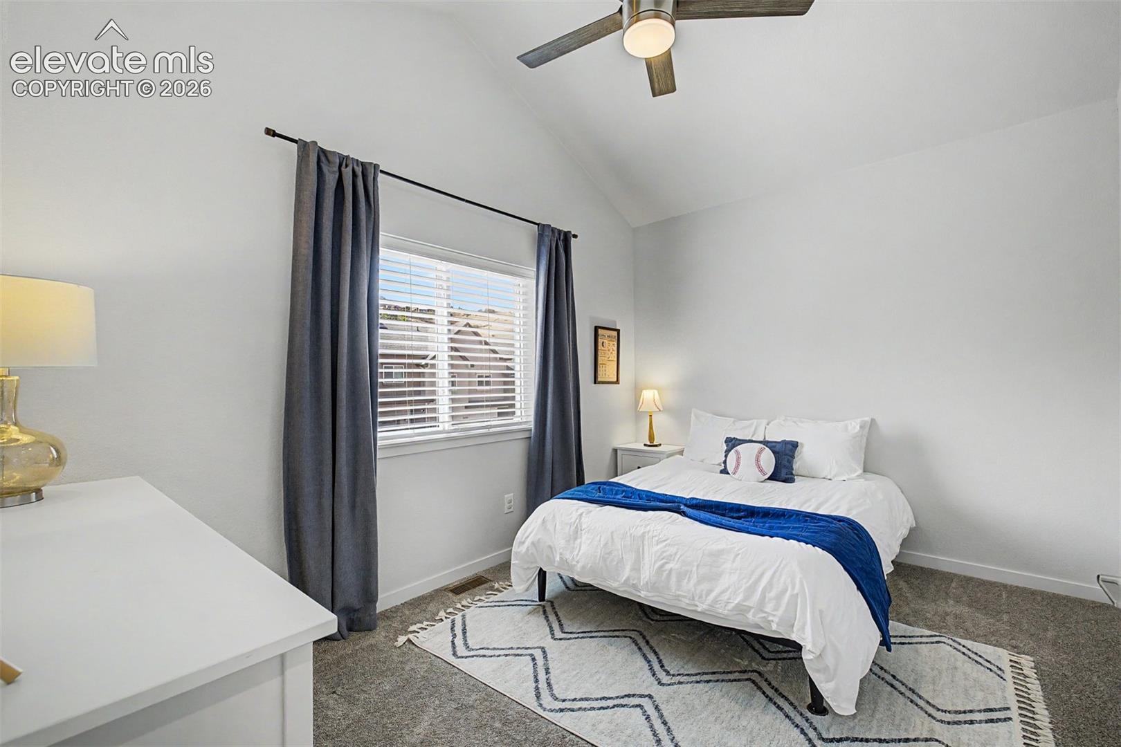 Vaulted ceilings give this cheerful secondary bedroom an airy, playful energy, with a curtained window and cozy carpet that makes it easy to imagine the life you could build within these walls.