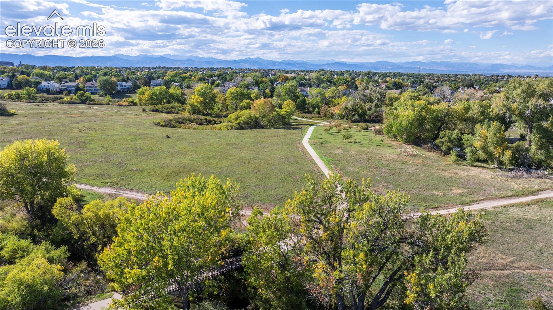 Expansive open space featuring mature trees, paved pedestrian paths, and mountain scenery