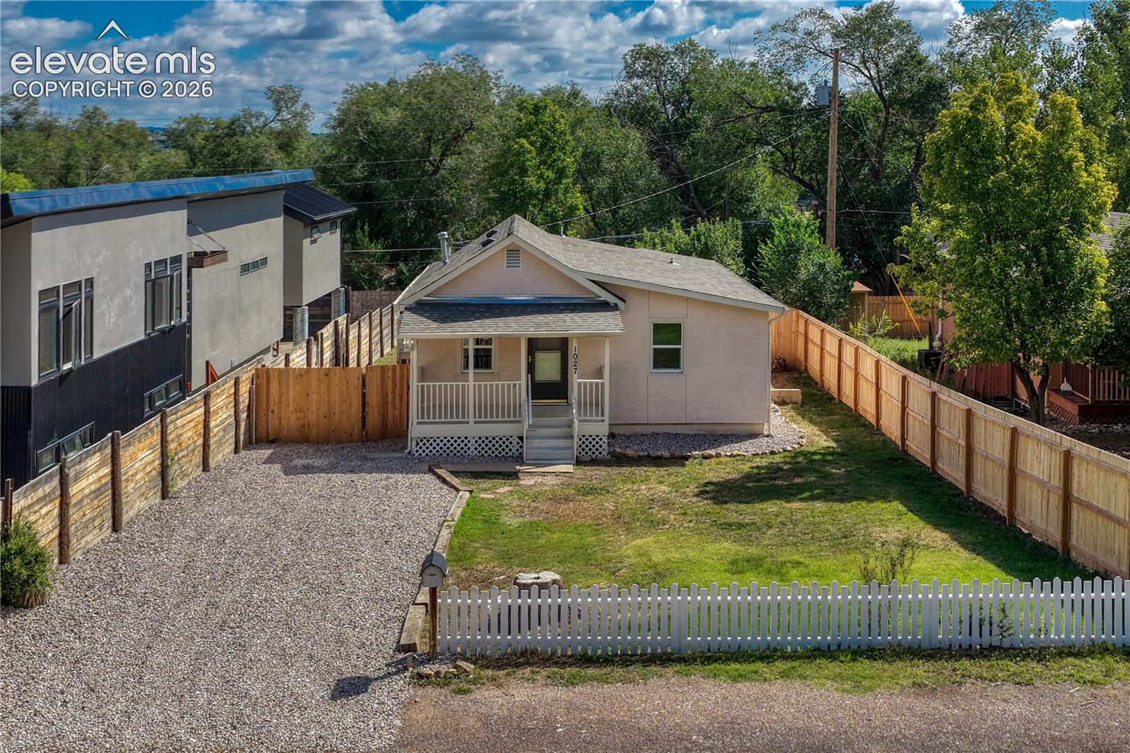 Gravel driveway, white picket fence, covered front porch, and expansive lawn area