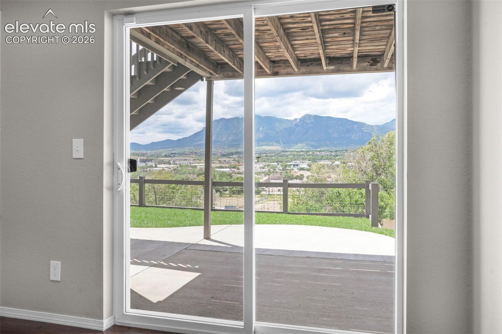 Sliding glass doors opening to an outdoor patio with mountain scenery and a wooden deck overhead
