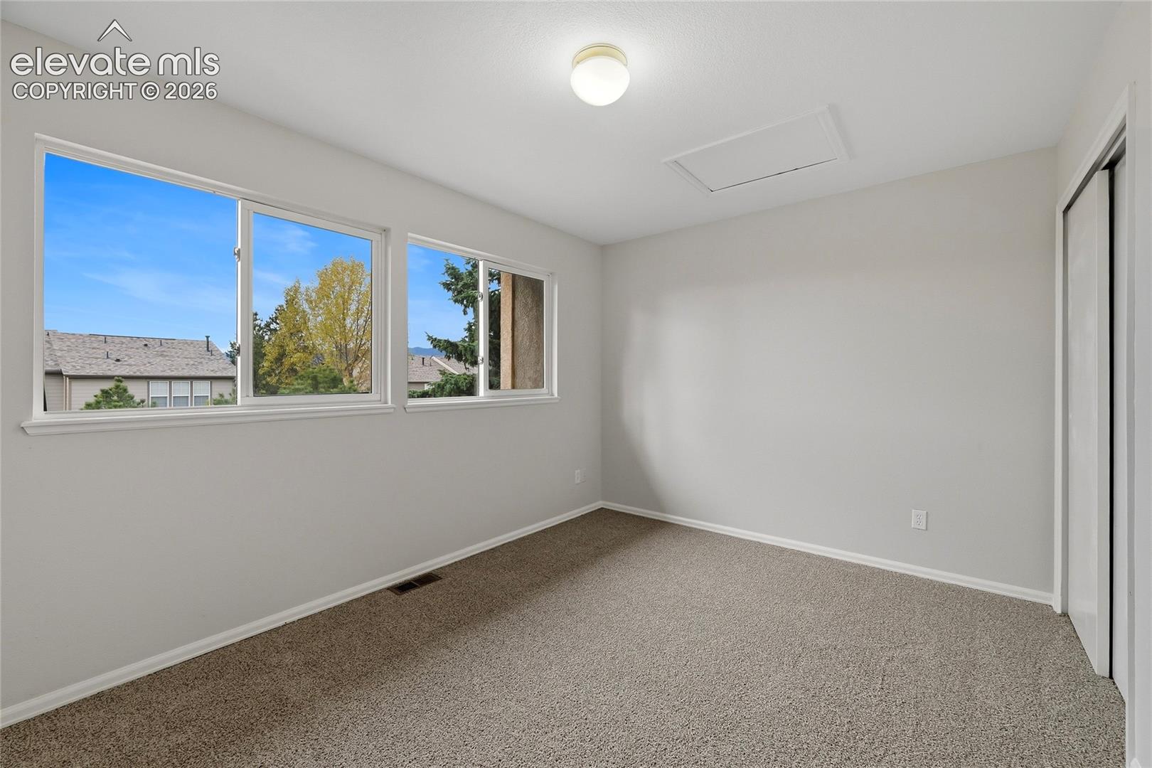 Neutral-toned interior space featuring dual sliding windows, neutral carpeting, and a closet with sliding doors