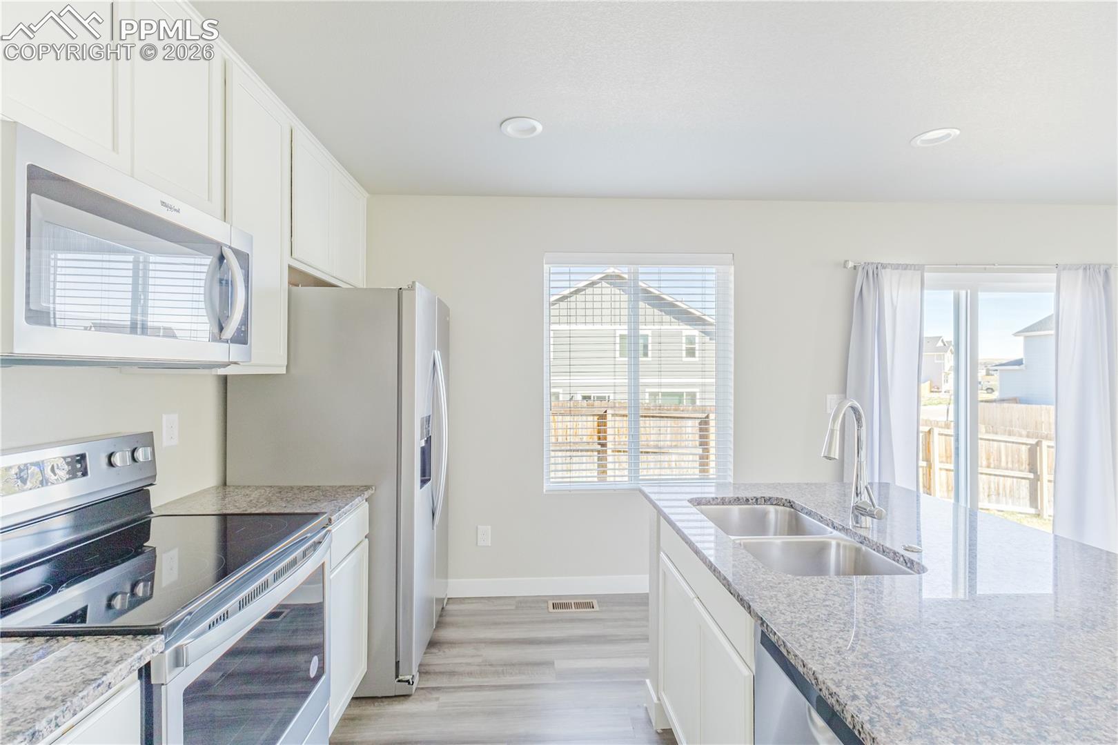 Kitchen featuring stainless steel appliances, white cabinetry, light wood-type flooring, light stone counters, and recessed lighting