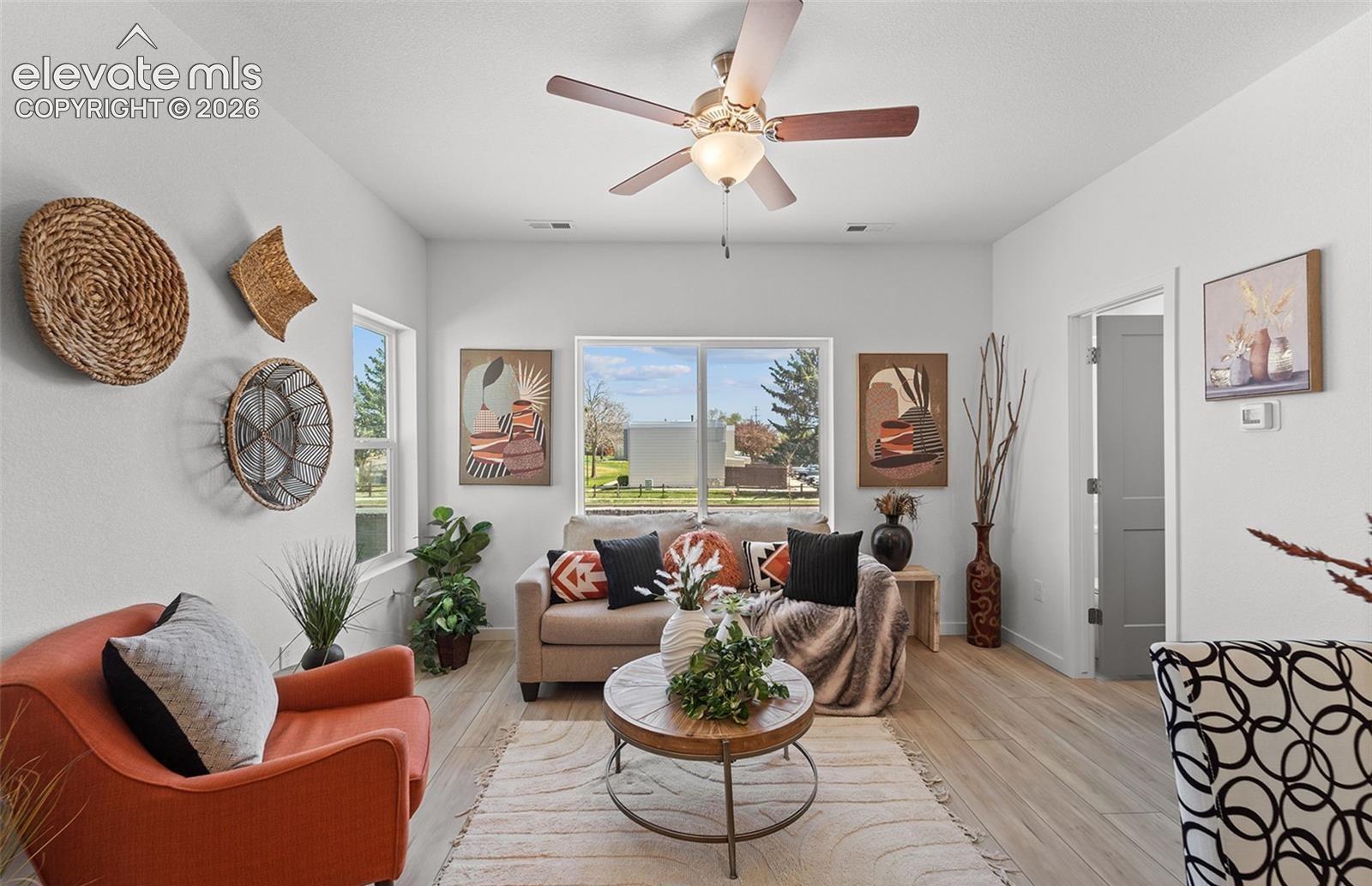 Living space featuring light wood-finish flooring, multi-pane windows, and a ceiling fan with integrated lighting