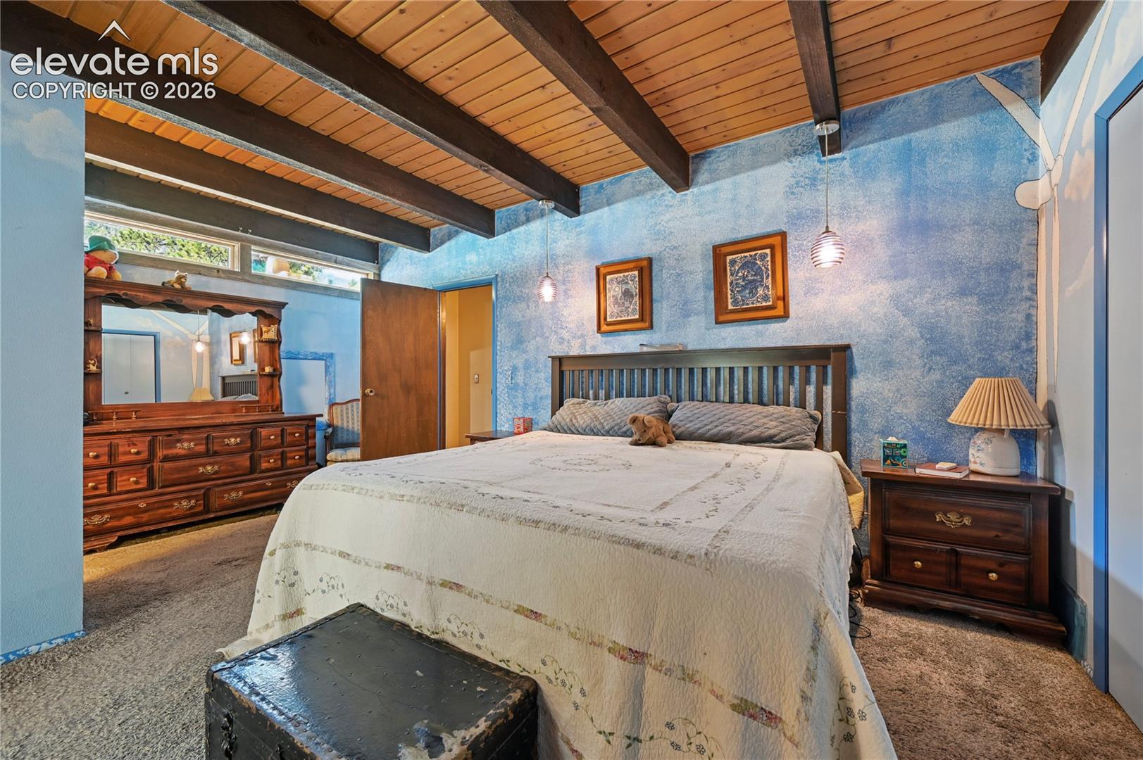 Main Bedroom, Exposed wood beam ceiling, blue textured wall finish, wood-finish flooring, transom windows, and built-in architectural elements