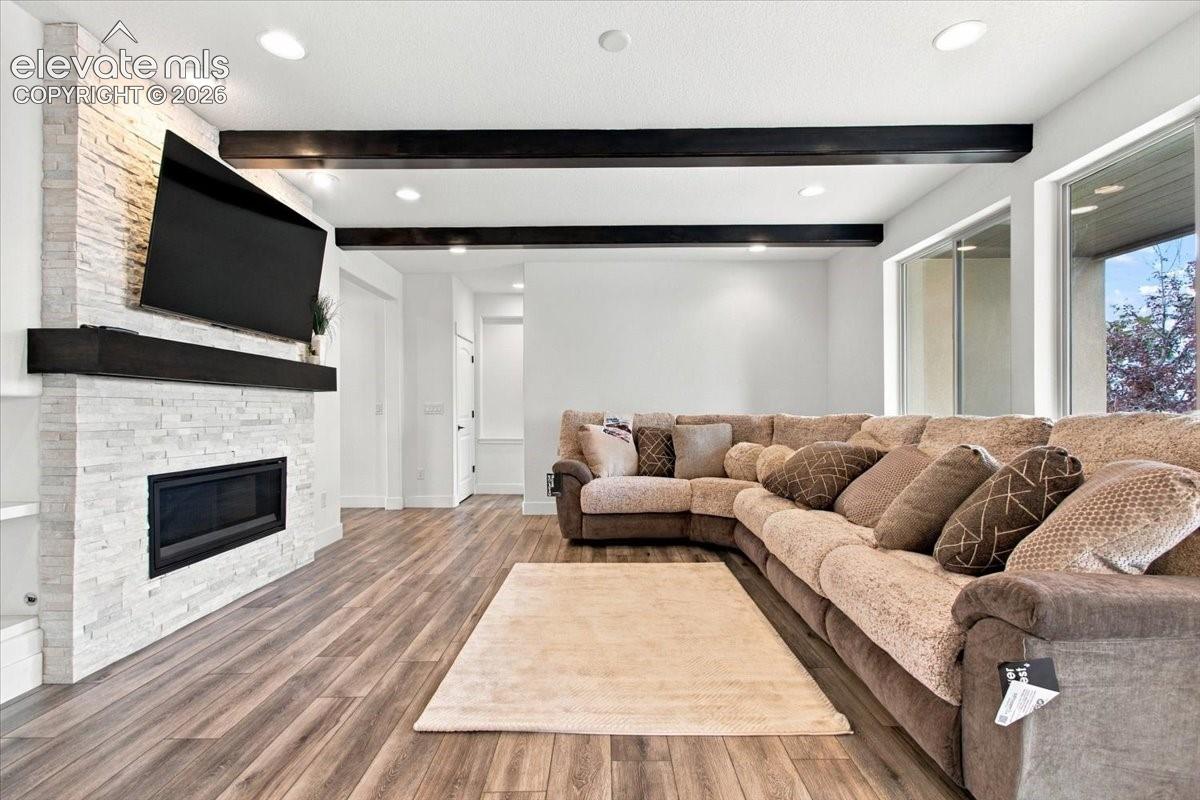 Floor-to-ceiling stone fireplace surround, recessed ceiling lighting, wood-finish flooring, and dark-stained exposed ceiling beams