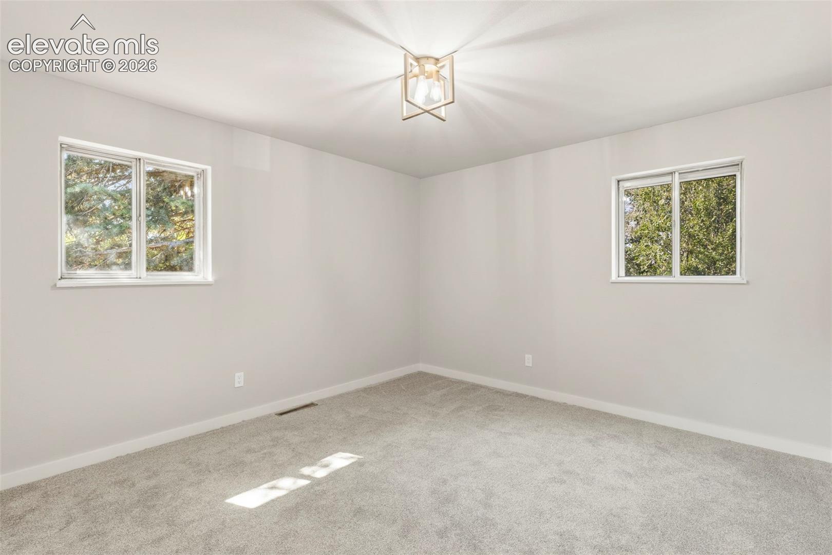Spacious room featuring light gray walls, plush carpeting, two windows, and a modern ceiling light fixture