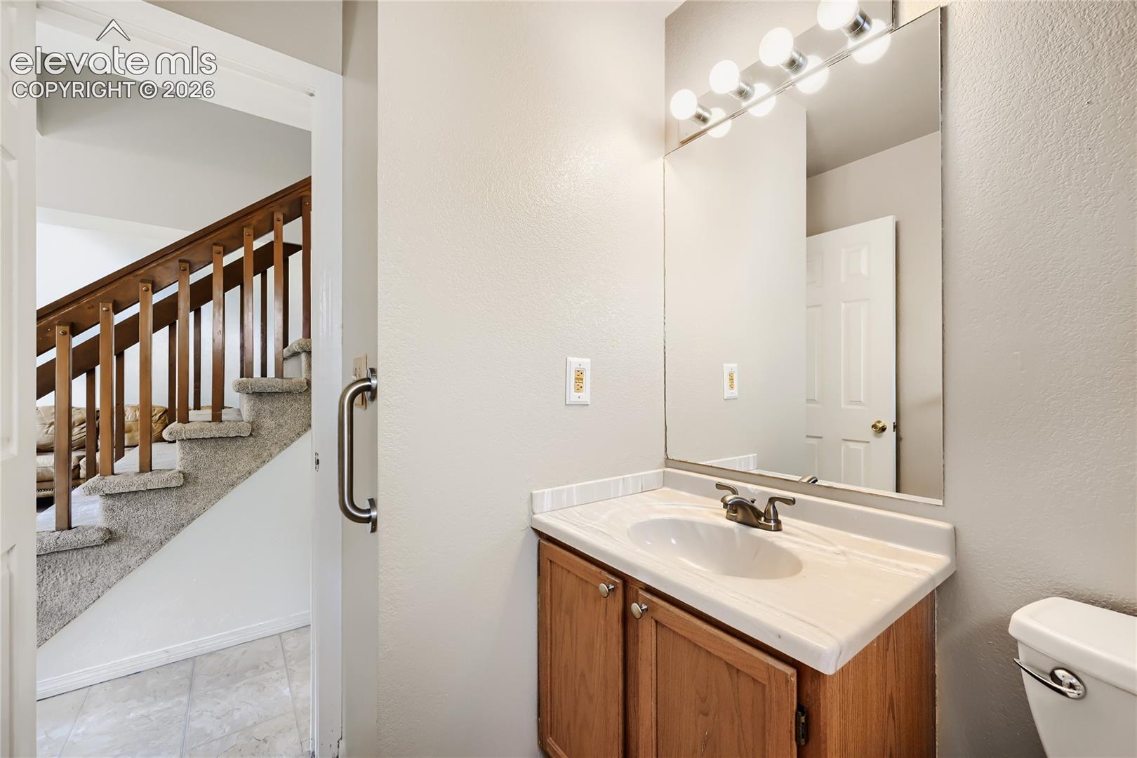 Bright bathroom featuring a wood-finish vanity with ample countertop space, white porcelain sink, and large mirror with integrated lighting