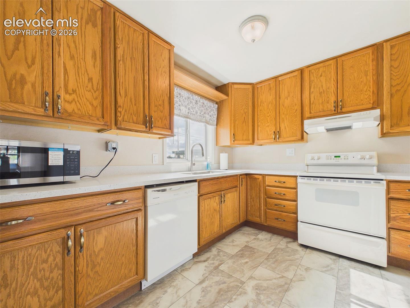 Functional kitchen featuring abundant oak cabinetry, generous counter space, white appliances, and easy access to the adjoining living area.