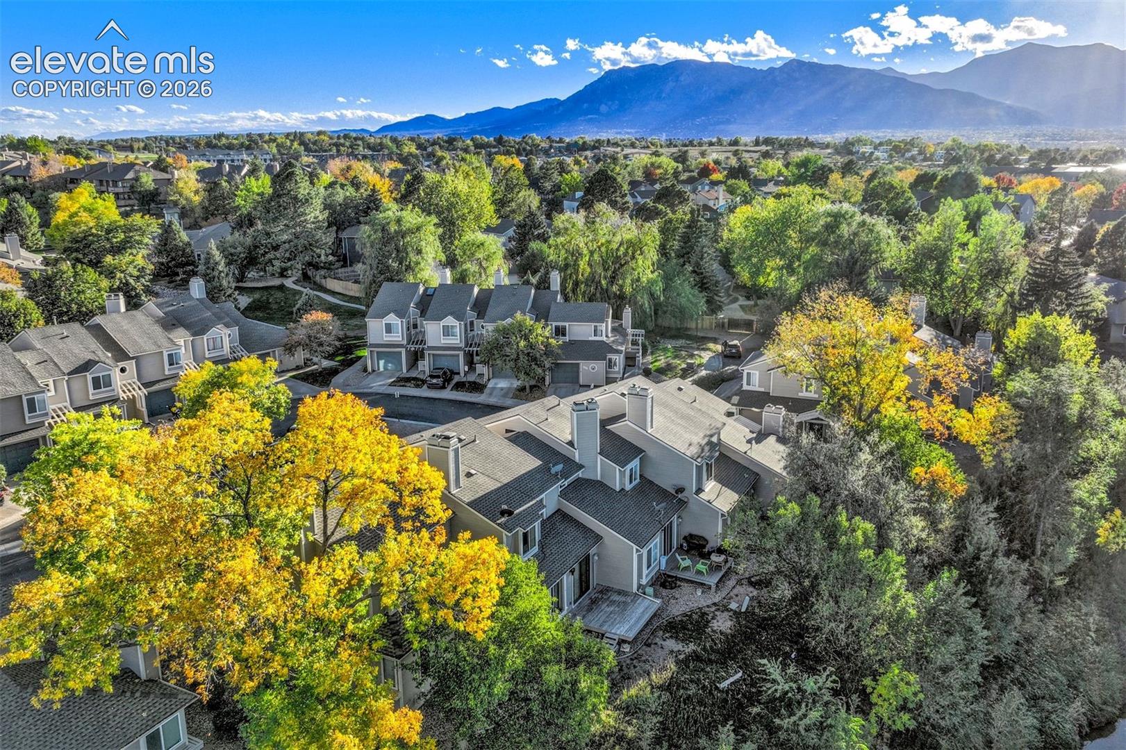 Aerial perspective featuring multi-level residential structures, wood decking, mature trees, and a mountain range backdrop