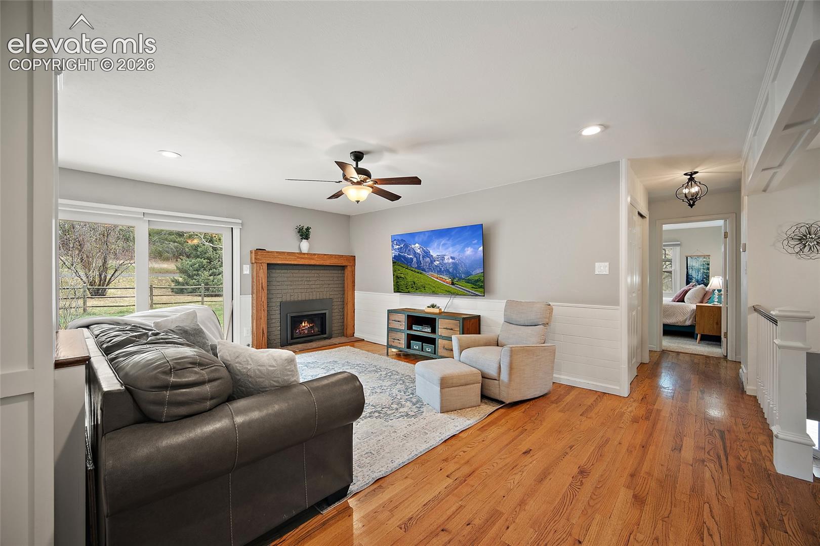 Living area featuring wood-finish flooring, a fireplace with a wood mantel and brick surround, wainscoting, and recessed lighting
