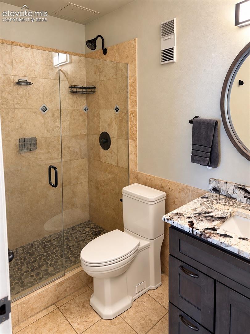 Glass-enclosed shower with stone tile surround and pebble flooring